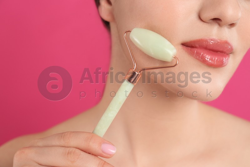 Photo of Woman using natural jade face roller on pink background, closeup