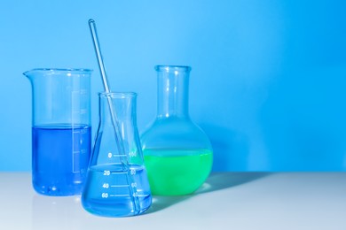Photo of Glass flasks with colorful liquids on white table against light blue background. Space for text