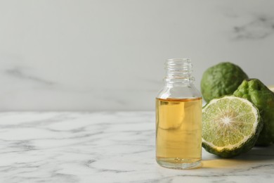 Photo of Bottle of essential oil and fresh bergamot fruits on white marble table. Space for text