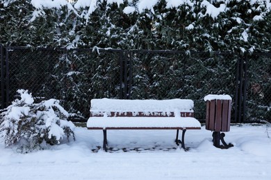 Photo of Trash bin and wooden bench covered with snow in morning park