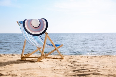 Photo of Lounger and hat on sand near sea, space for text. Beach objects