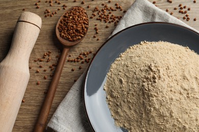 Plate with buckwheat flour, grains and rolling pin on wooden table