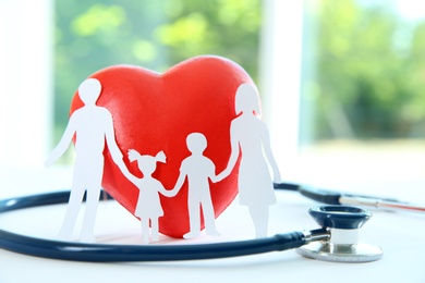 Red heart model, stethoscope and paper family cutout on table, closeup