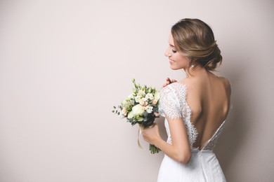 Young bride with elegant hairstyle holding wedding bouquet on beige background. Space for text