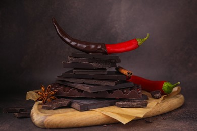Photo of Red hot chili peppers and pieces of dark chocolate with spices on grey table
