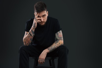 Photo of Handsome hipster man posing on chair against black background. Space for text