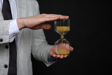 Closeup view of businessman holding hourglass on black background, space for text. Time management