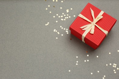 Red gift box and shiny confetti on grey background, above view. Space for text