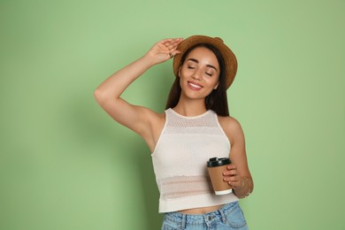Beautiful young woman with straw hat and cup of coffee on olive background. Stylish headdress