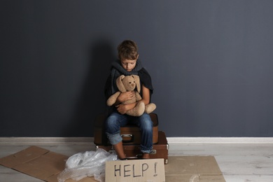 Poor boy with toy asking for help near dark wall