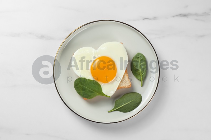 Romantic breakfast with heart shaped fried egg on white marble table, top view