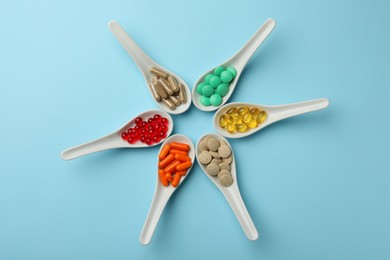 Spoons with different dietary supplements on light blue background, flat lay