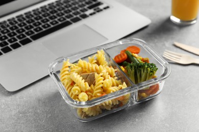Photo of Container with tasty food, laptop and cutlery on light grey table. Business lunch