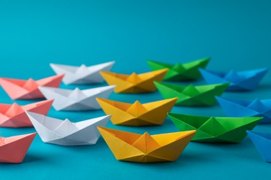 Many colorful handmade paper boats on light blue background. Origami art