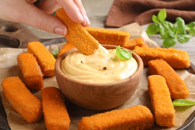Photo of Woman dipping delicious chicken nuggets into cheese sauce at table, closeup