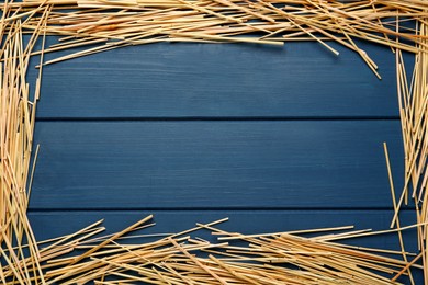 Frame of dried hay on blue wooden background, flat lay. Space for text