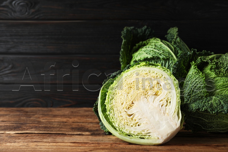 Photo of Whole and cut fresh ripe savoy cabbages on wooden table, space for text
