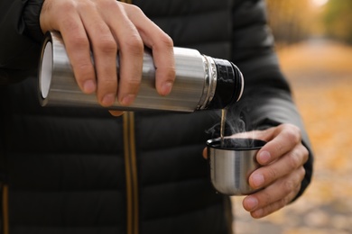 Man pouring drink from thermos into cap outdoors, closeup