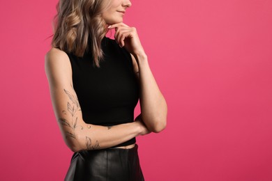 Photo of Beautiful woman with tattoos on arm against pink background, closeup. Space for text