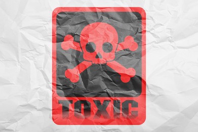 Image of Hazard warning sign (skull-and-crossbones symbol and word TOXIC) on crumpled white paper, top view