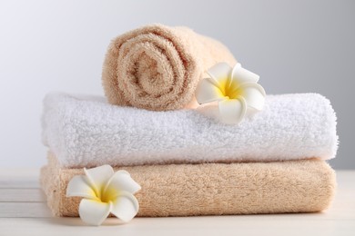 Photo of Closeup view of soft folded towels and plumeria flowers on white wooden table