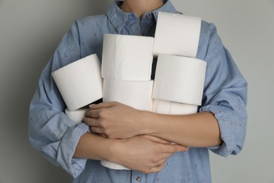 Woman with heap of toilet paper rolls on grey background, closeup