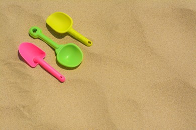 Photo of Colorful plastic shovels on sand, space for text. Beach toys