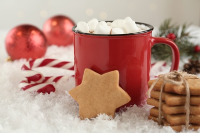 Hot drink with marshmallows in red cup, cookies and candy canes on snow
