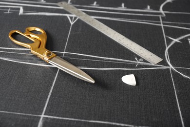 Scissors, tailor's chalk and ruler on grey fabric with sewing patterns