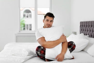 Young man with soft pillow on bed at home
