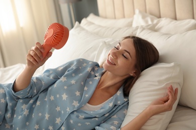 Woman enjoying air flow from portable on bed in room. Summer heat