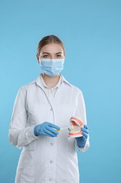 Dental assistant with jaws model and toothbrush on light blue background. Oral care demonstration