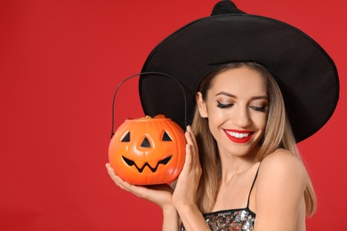 Beautiful woman wearing witch costume with Jack O'Lantern candy container on red background. Halloween party