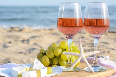 Glasses with rose wine and snacks on sandy seashore, closeup. Space for text
