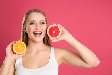 Emotional young woman with cut orange and grapefruit on pink background. Vitamin rich food