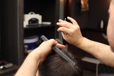 Professional hairdresser cutting man's hair in barbershop, closeup