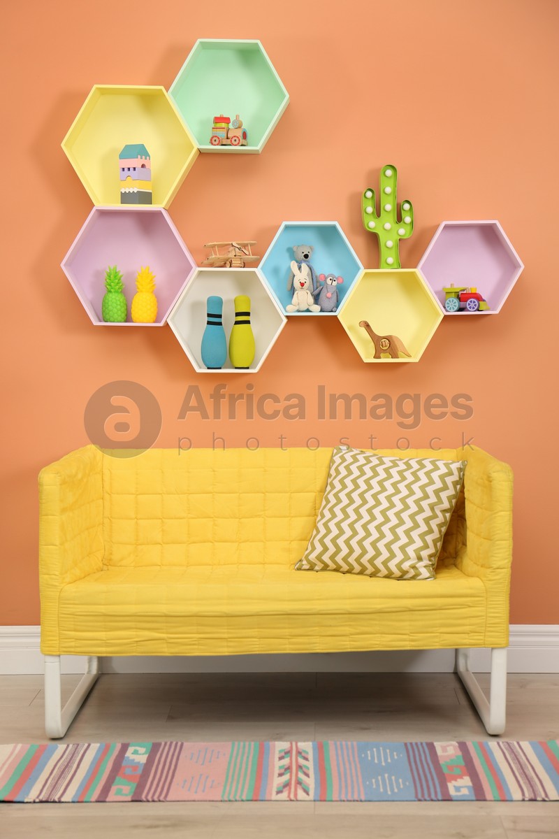 Sofa near orange wall with hexagon shaped shelves in room. Interior design
