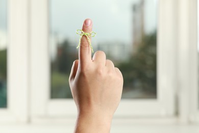 Man showing index finger with tied bow as reminder near window indoors, closeup