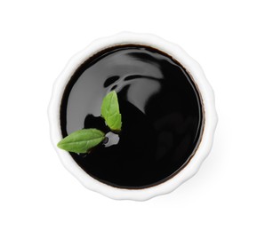 Photo of Balsamic glaze with basil leaves in bowl isolated on white, top view
