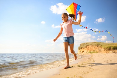 Cute little child with kite running on beach near sea. Spending time in nature