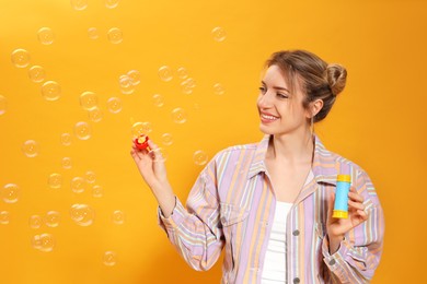 Young woman blowing soap bubbles on yellow background, space for text