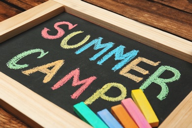 Little blackboard with text SUMMER CAMP chalked in different colors on table