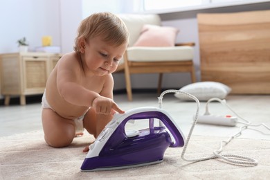 Photo of Cute baby playing with iron on floor at home. Dangerous situation