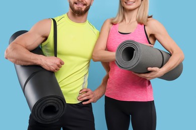 Photo of Athletic people with fitness mats on light blue background, closeup
