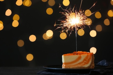 Cake with burning sparkler on black table against blurred festive lights. Space for text