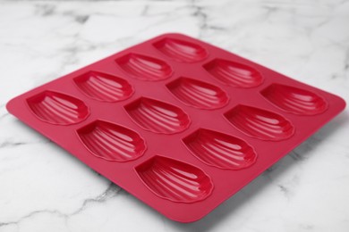 Photo of Red baking mold for madeleine cookies on white marble table, closeup