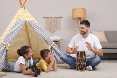 Father and children playing near toy wigwam at home