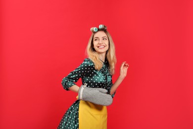 Young housewife with hair curlers on red background