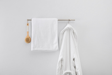 Rack with clean bathrobe, brush and towel on light wall