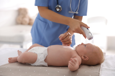 Doctor measuring temperature of little baby with non-contact thermometer in clinic, closeup. Health care